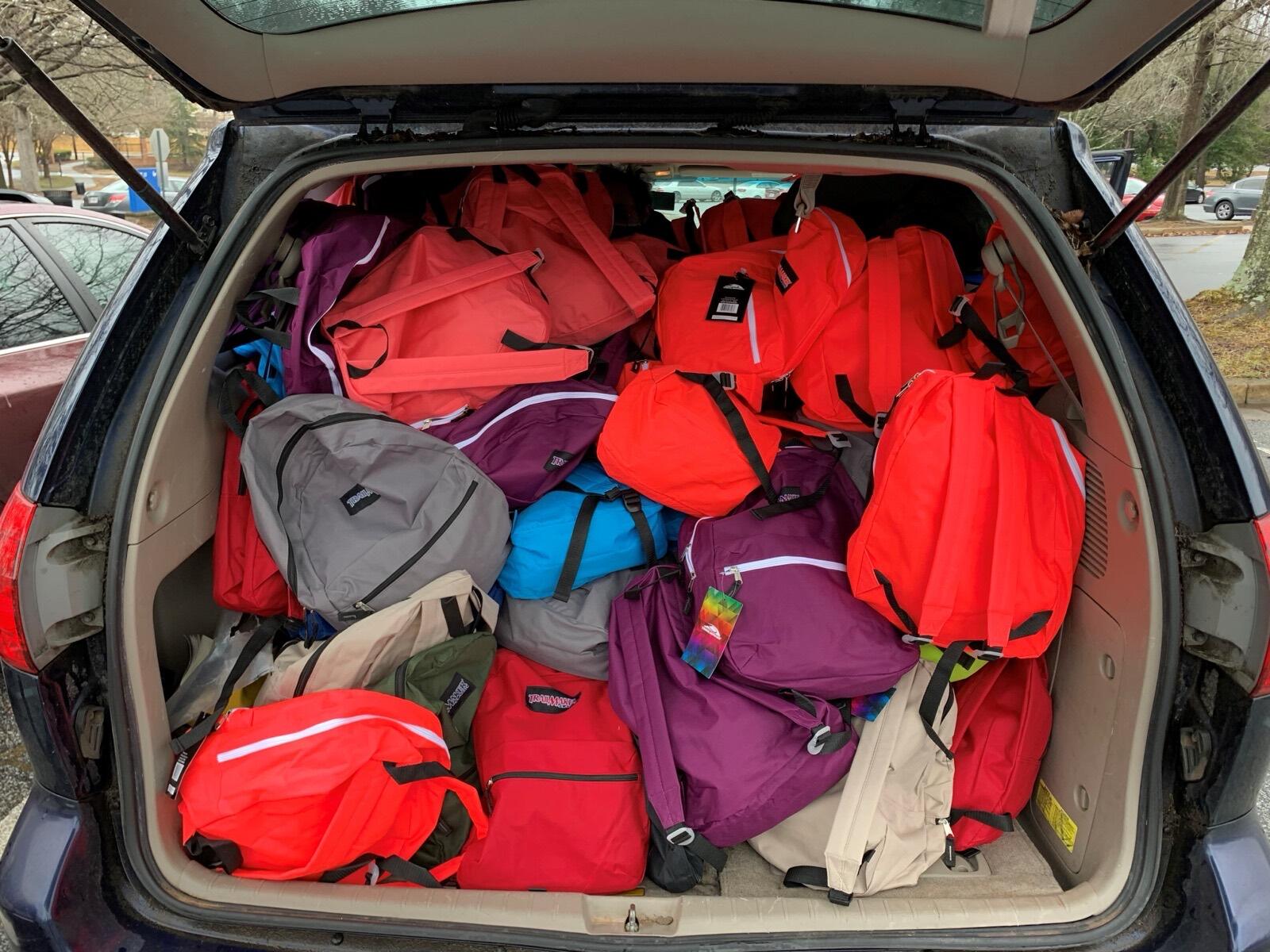 The back of a car packed full of colorful backpacks ready for delivery.