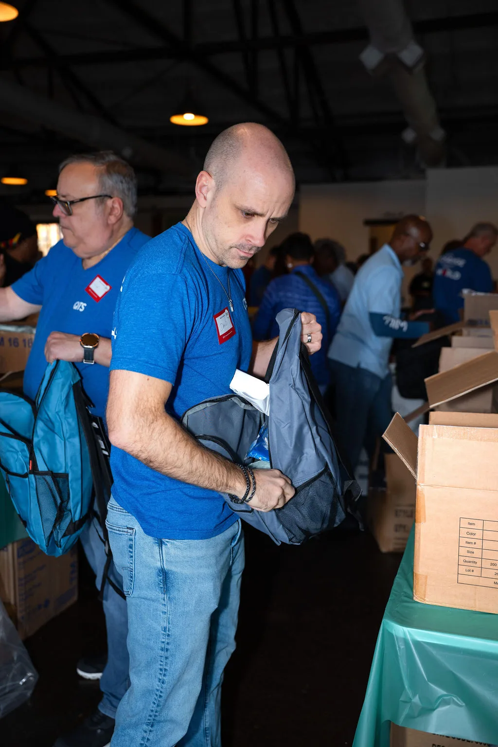 A volunteer fills a gray backpack from a supply table at Homeless Heroes Day 2025.