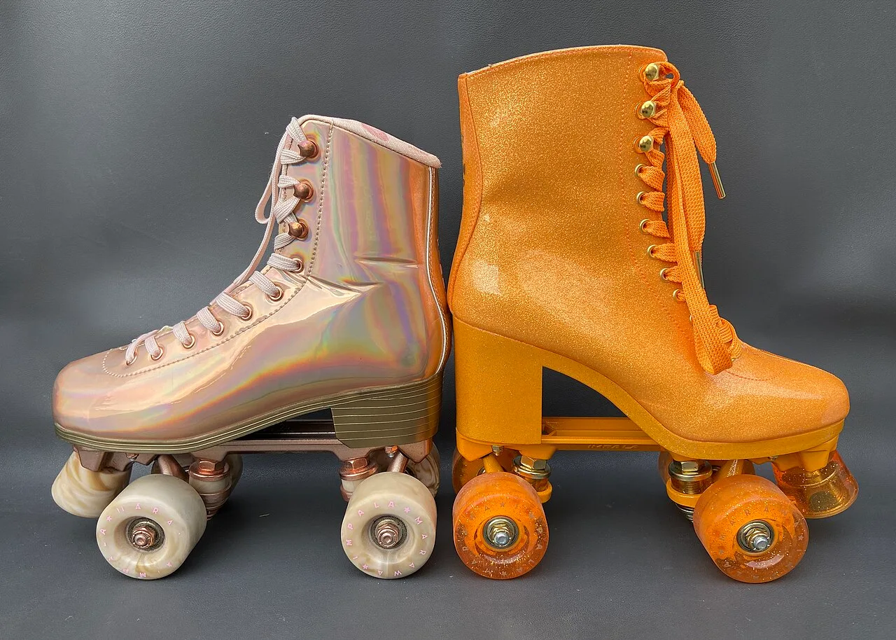 Two quad roller skates shown side by side in profile — one iridescent pale pink and one bright orange — on a plain neutral background.