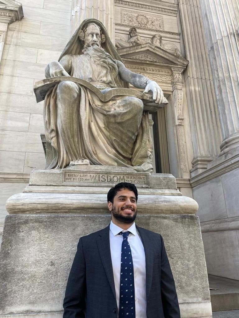 Nisheet Dabadge poses at the foot of an old statue, wearing a dark blue suit