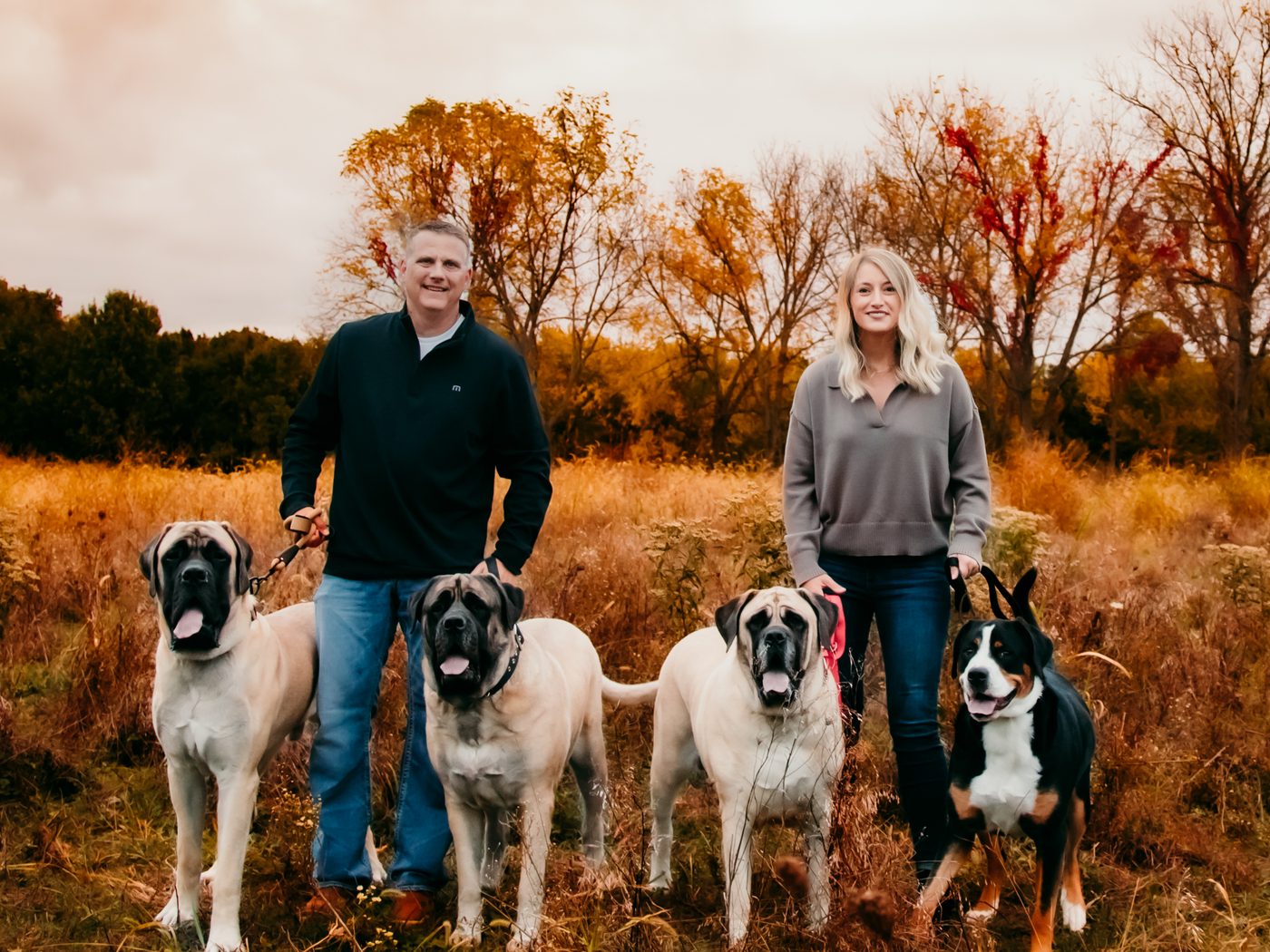 Trisha and her husband with their four dogs in a fall field