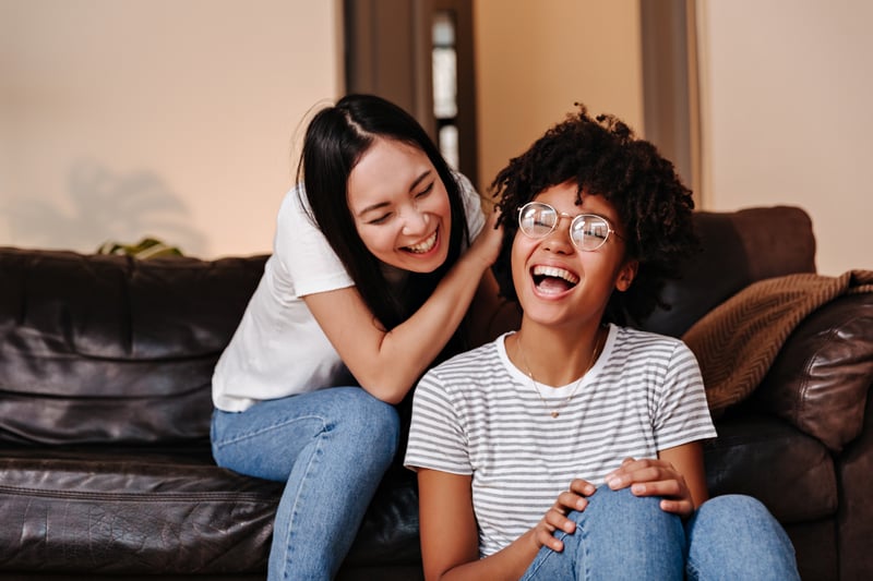 Two friends laughing together on a living room couch