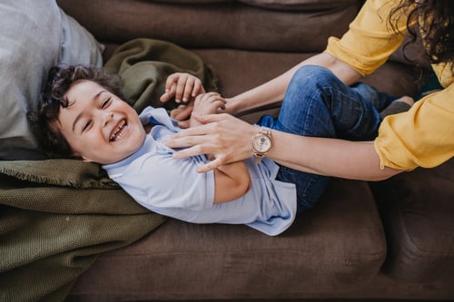 A parent tickling a laughing child on the couch