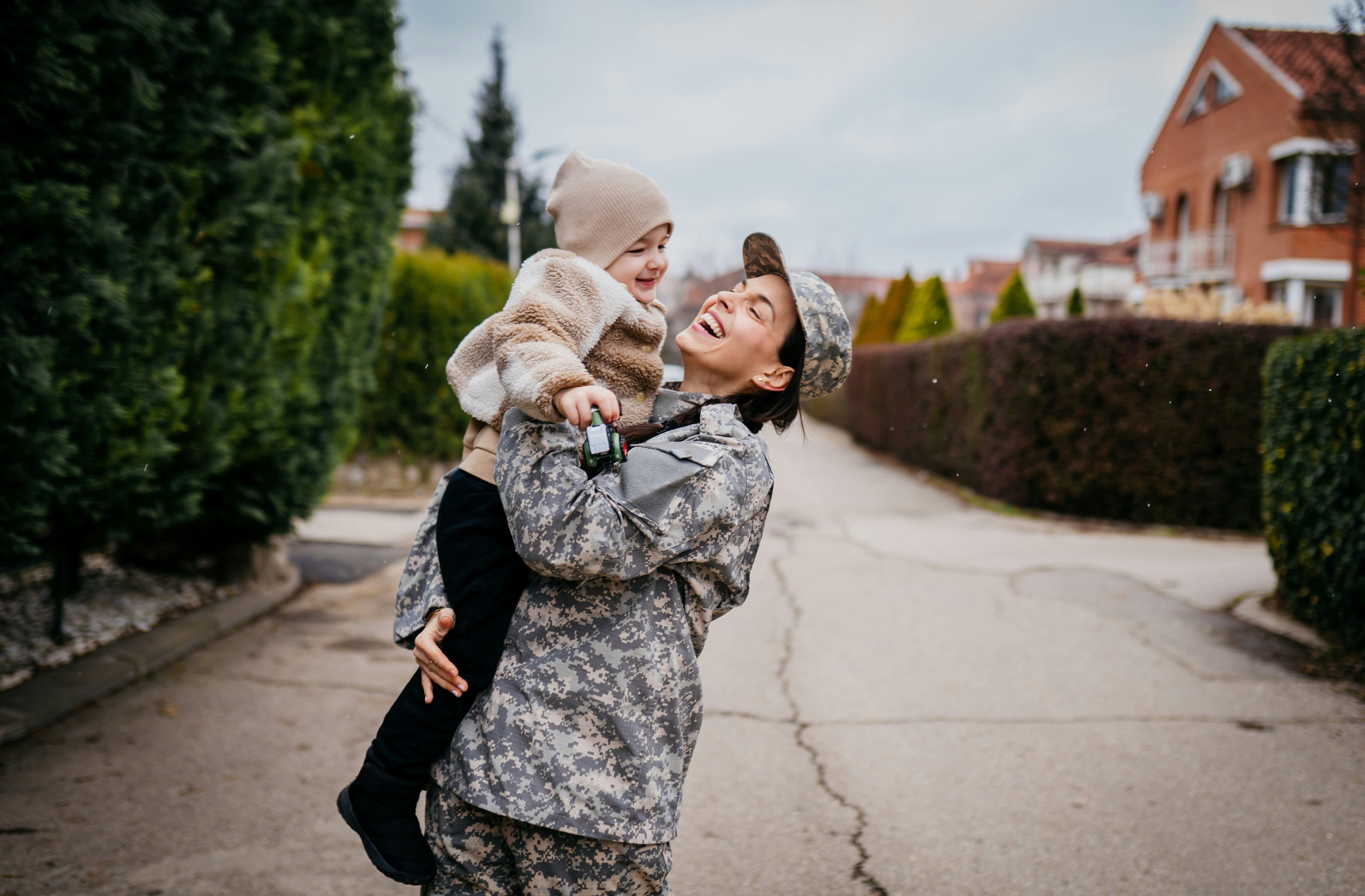 A service member in uniform holding a child on a neighborhood street