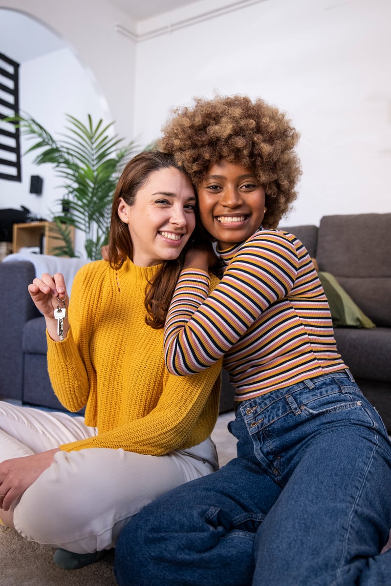 Two friends hugging on the living room floor, one holding house keys