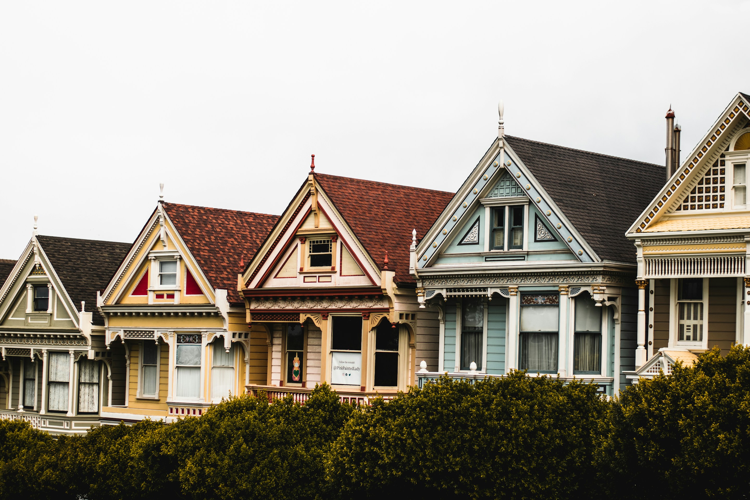 A row of colorful Victorian houses behind green hedges