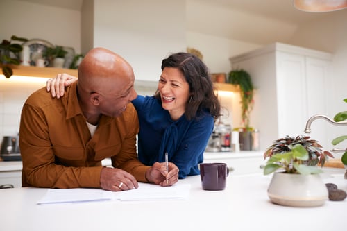 A smiling couple reviewing paperwork at their kitchen counter