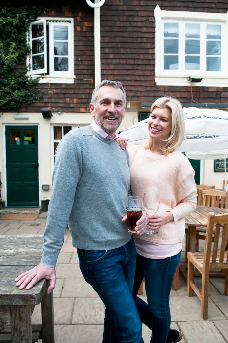 A smiling couple standing on a patio outside a brick building