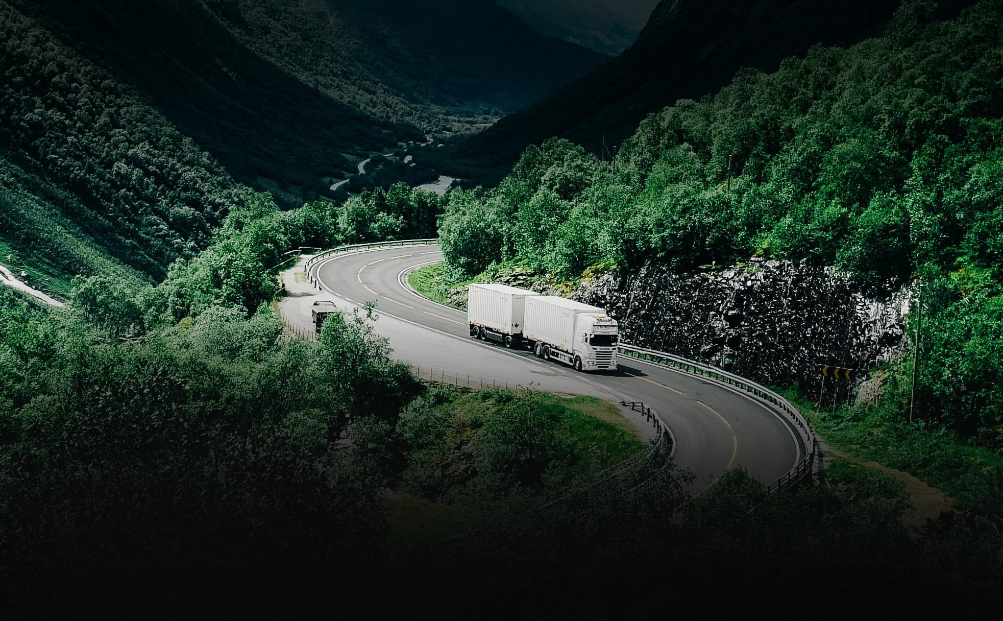 Lorry travelling along a winding road through a wooded valley