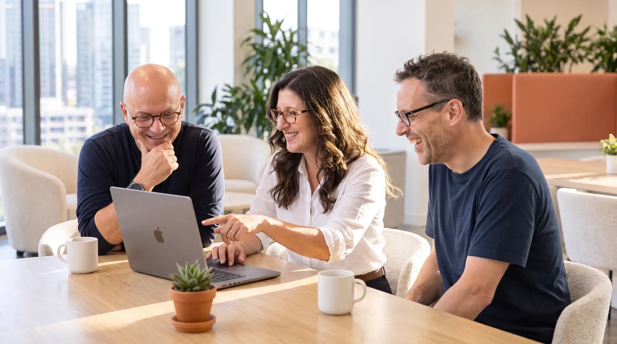 The Synthrics team laughing together while reviewing work on a laptop