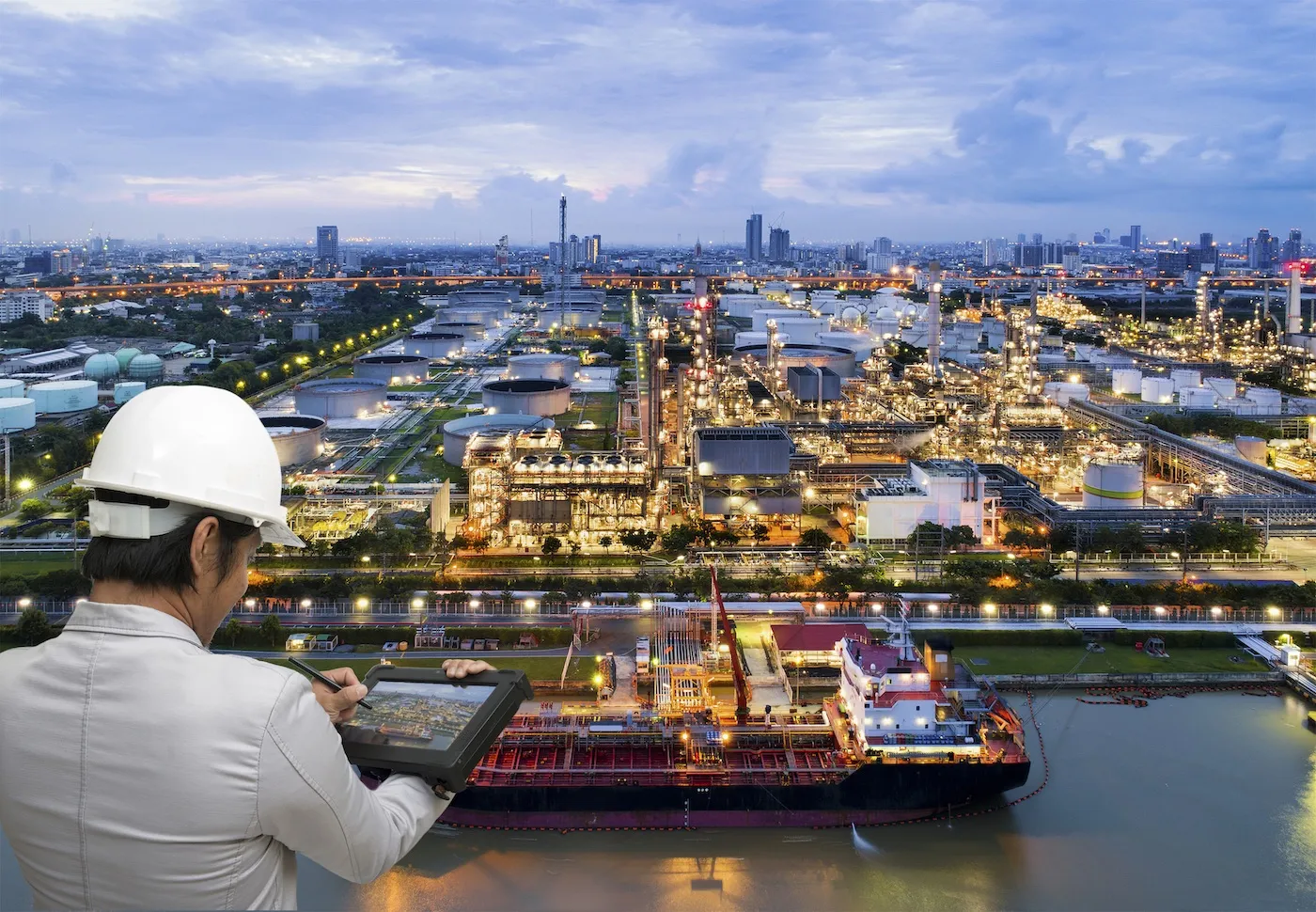 Engineer using a tablet above a refinery and tanker terminal at dusk