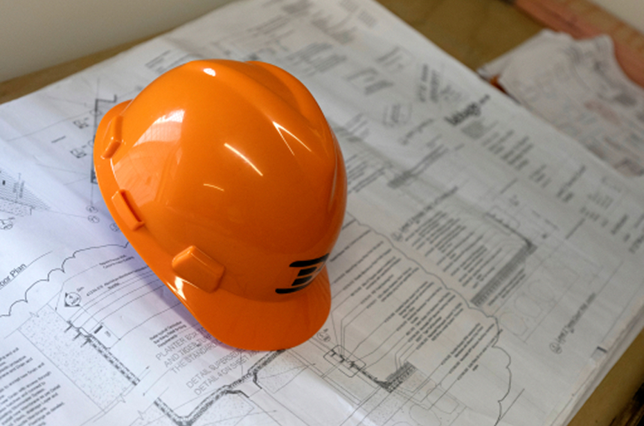 Orange construction helmet resting on detailed architectural blueprints on a wooden surface.