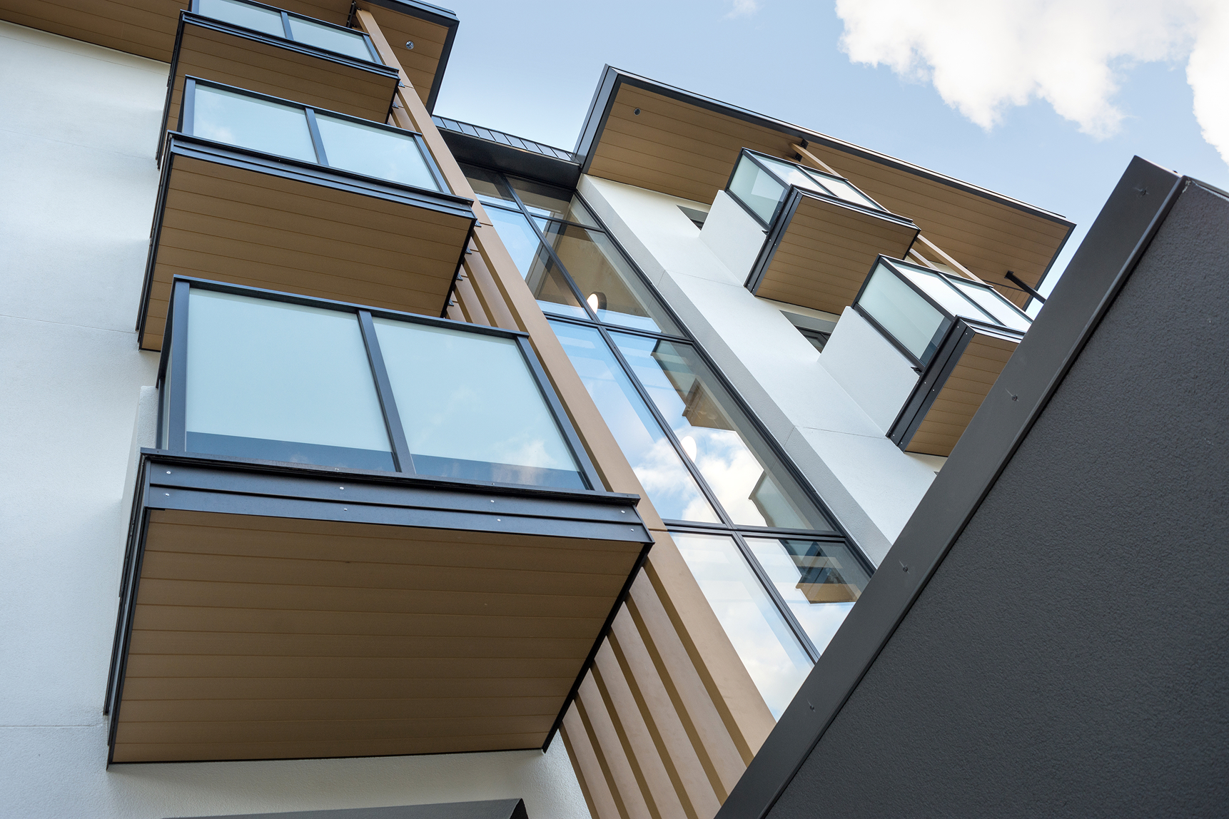 Upward view of modern apartment building balconies with glass railings and wooden accents.