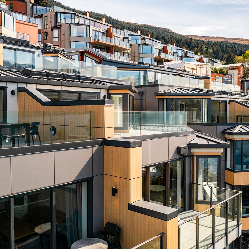 Modern multi-level apartments with glass balconies and wooden paneling overlooking a forested hillside.