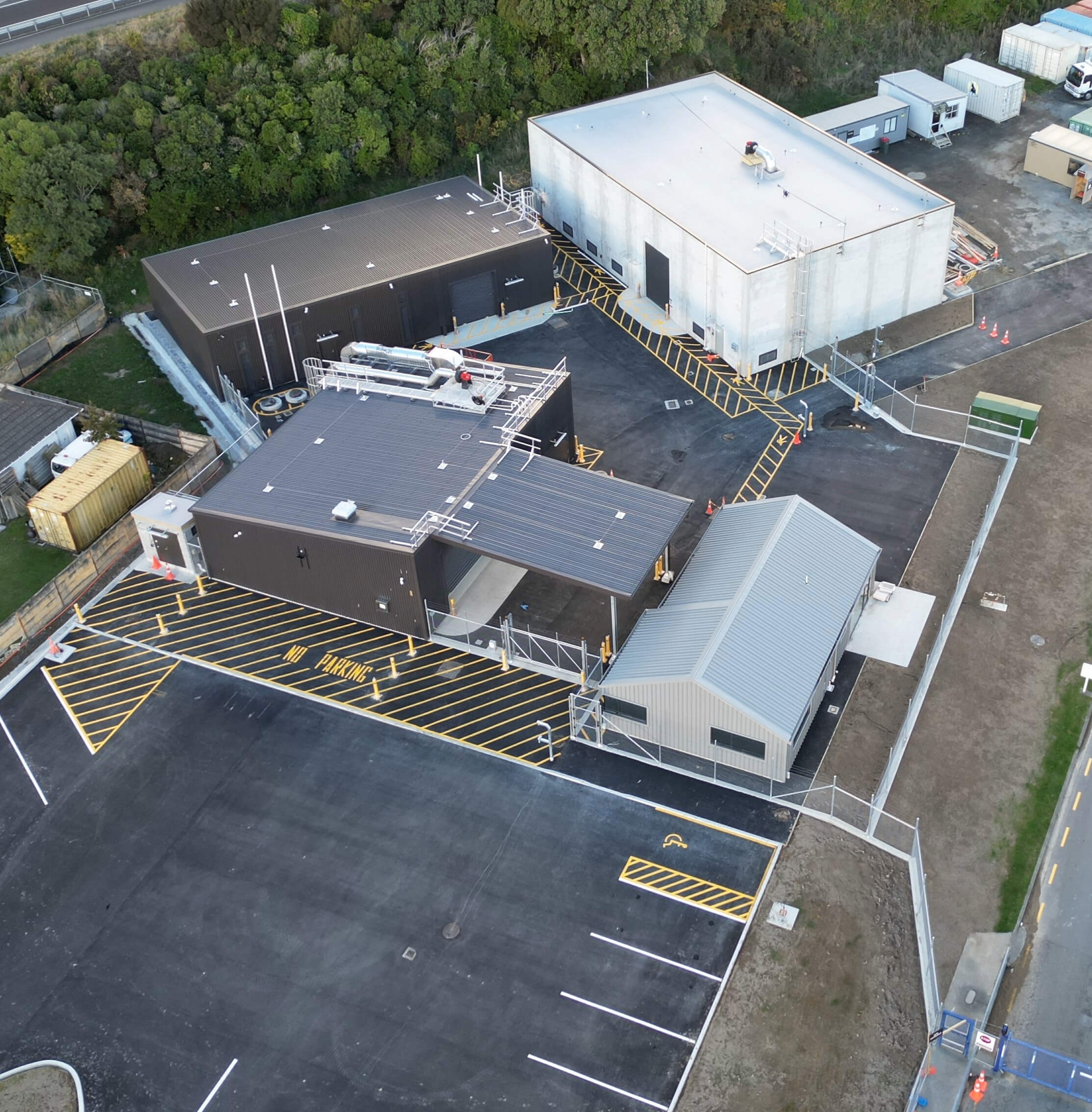 Aerial view of a fenced industrial complex with multiple buildings and marked parking areas.