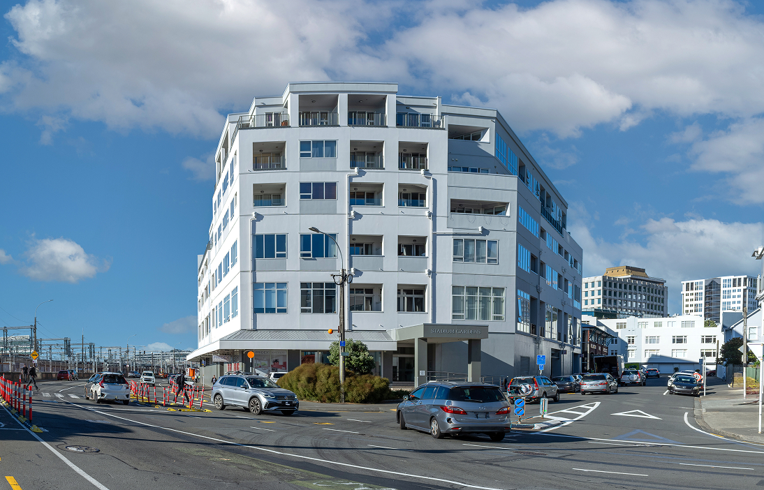 White multi-story building with commercial ground floor and cars on street on a clear day.