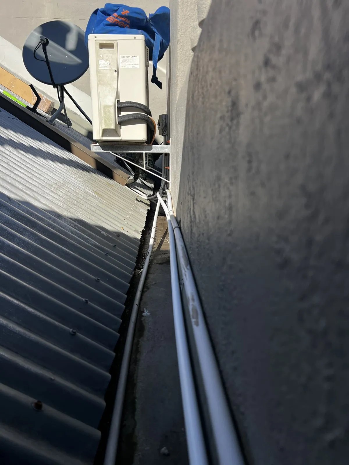 Gutter maintenance in progress beside a wall-mounted air-conditioning unit