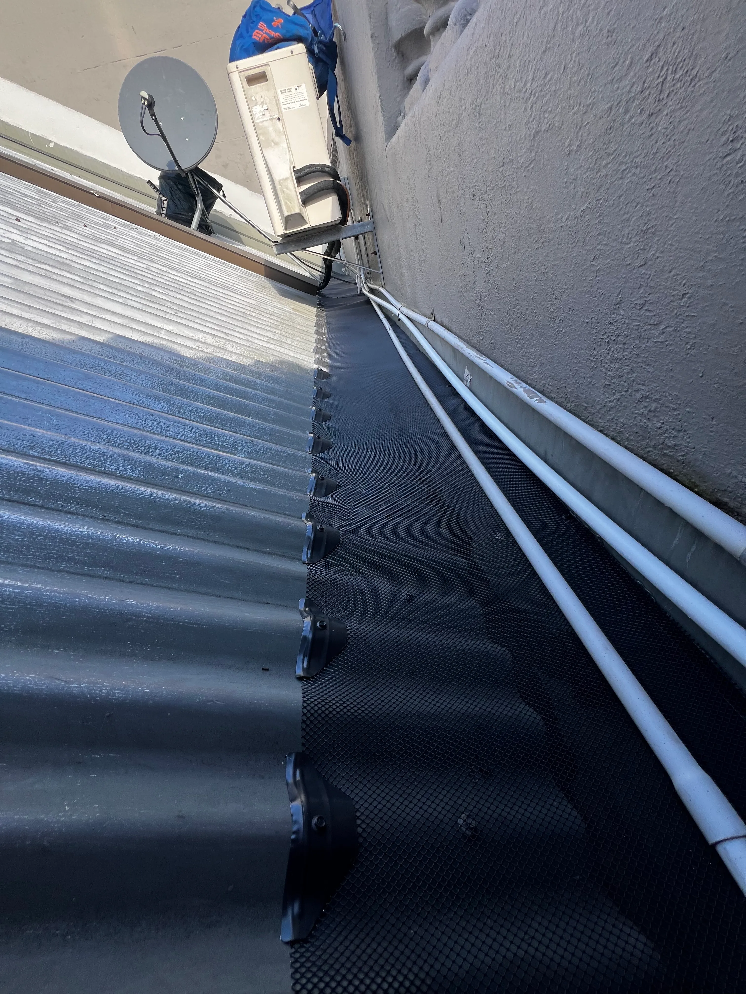Gutter guard mesh fitted beside a wall-mounted air-conditioning unit