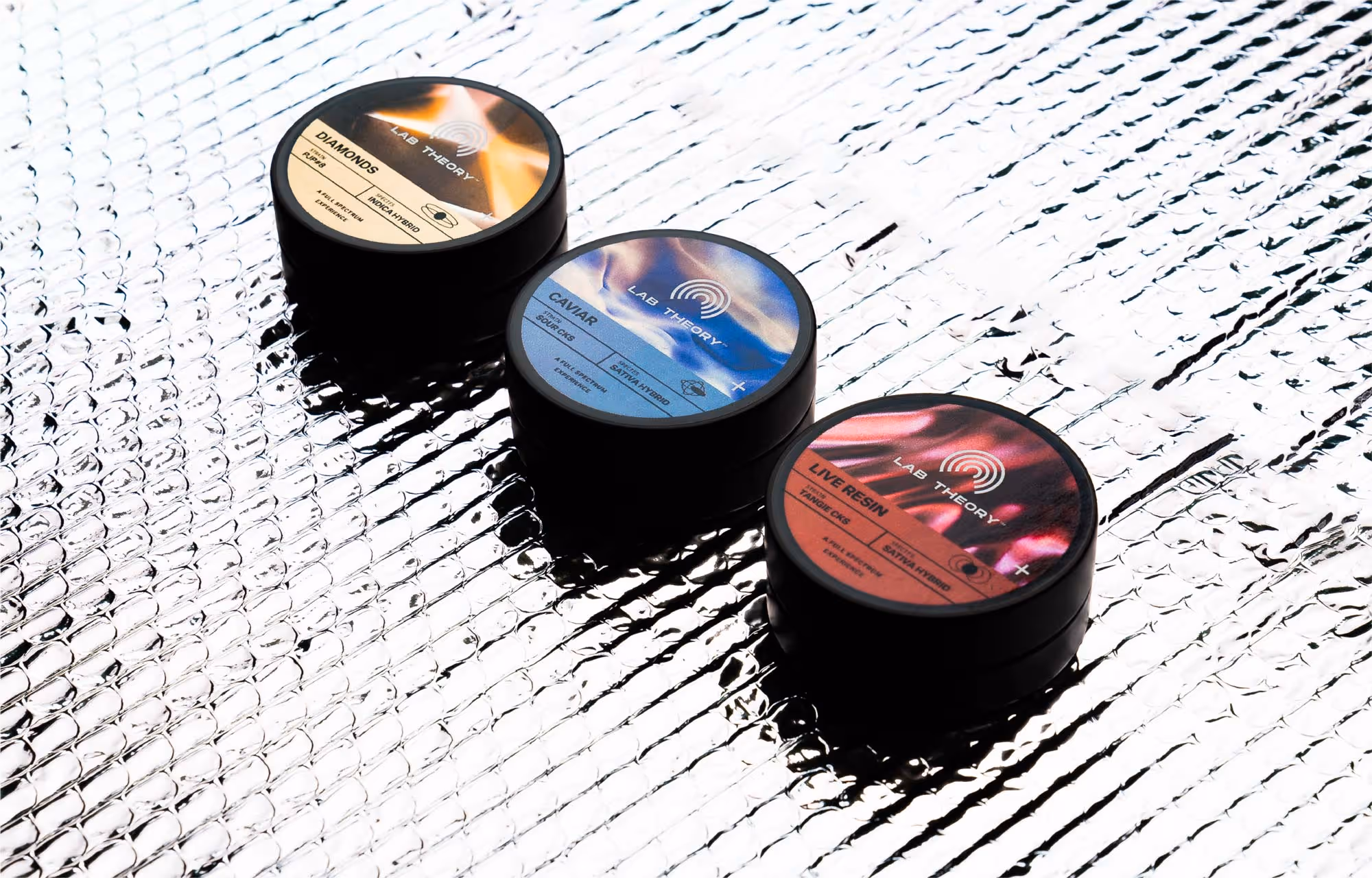 Three black round containers labeled Lab Theory, arranged diagonally on a textured reflective surface with labels reading Diamonds, Caviar, and Live Resin.