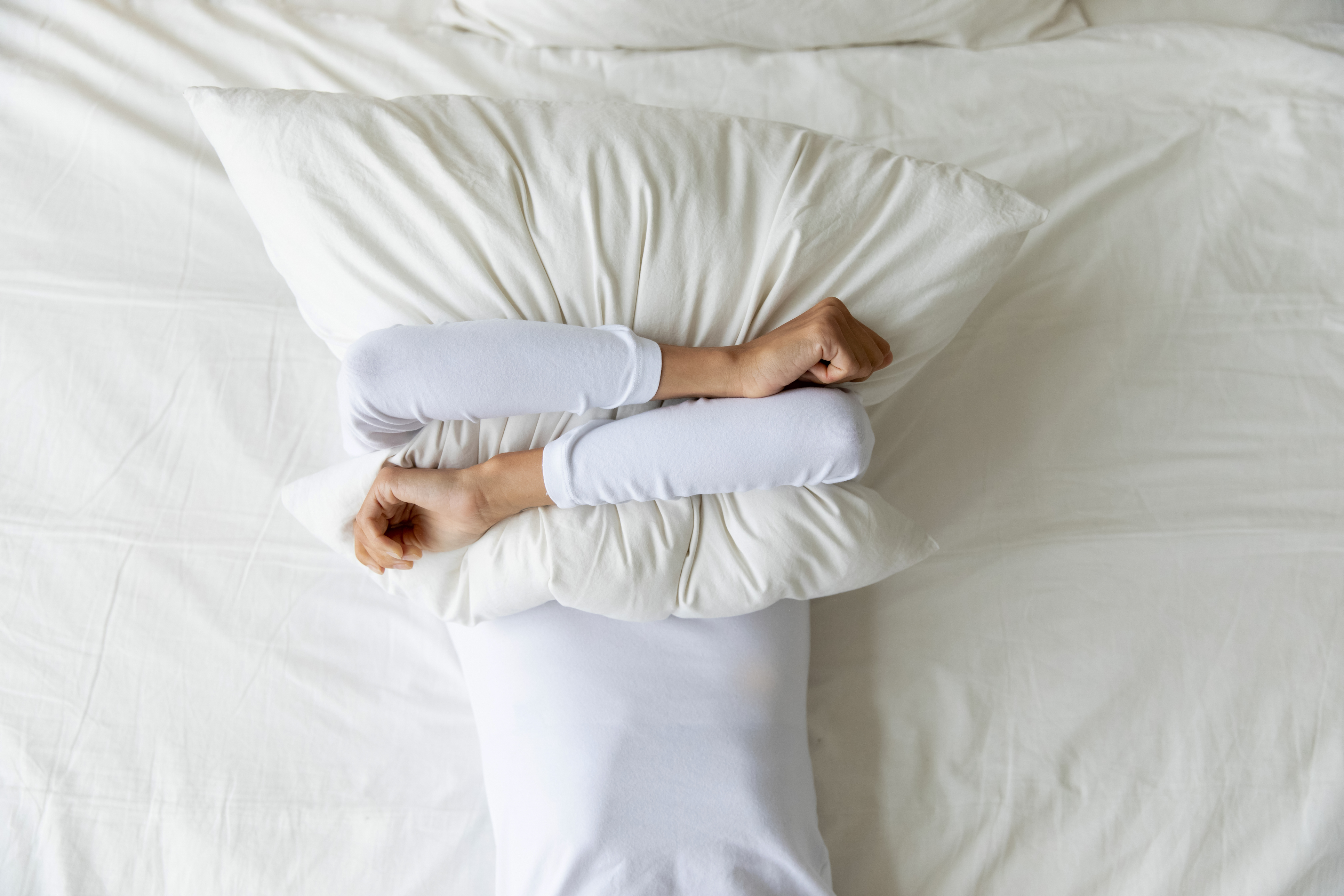 Person lying in bed hugging a pillow over their face