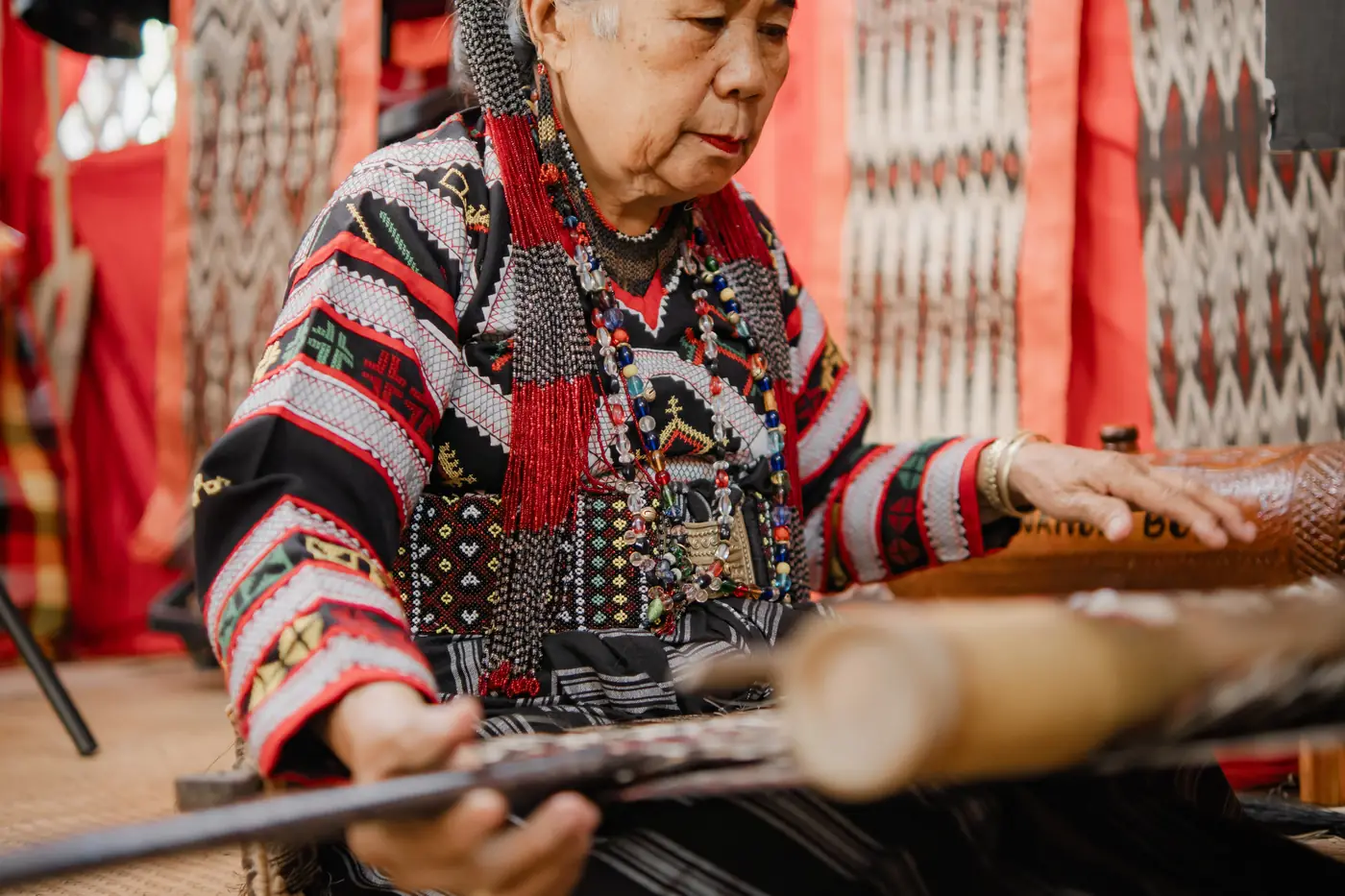 An elder weaver in traditional dress working a T’nalak at the loom