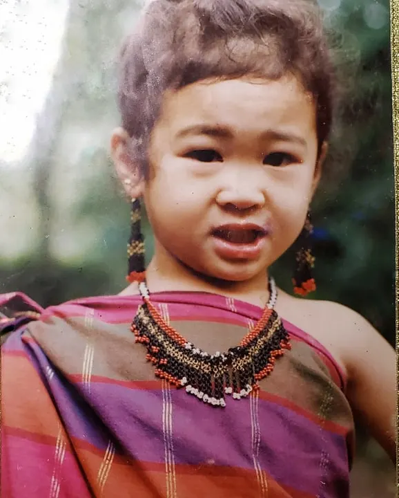 Cecille as a toddler, wearing a beaded necklace and earrings