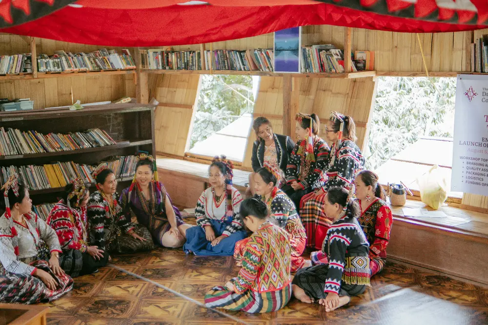 Weavers in traditional dress seated in a circle in the weaving center library