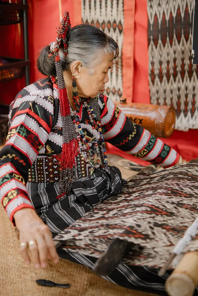 An elder weaver seated at her loom