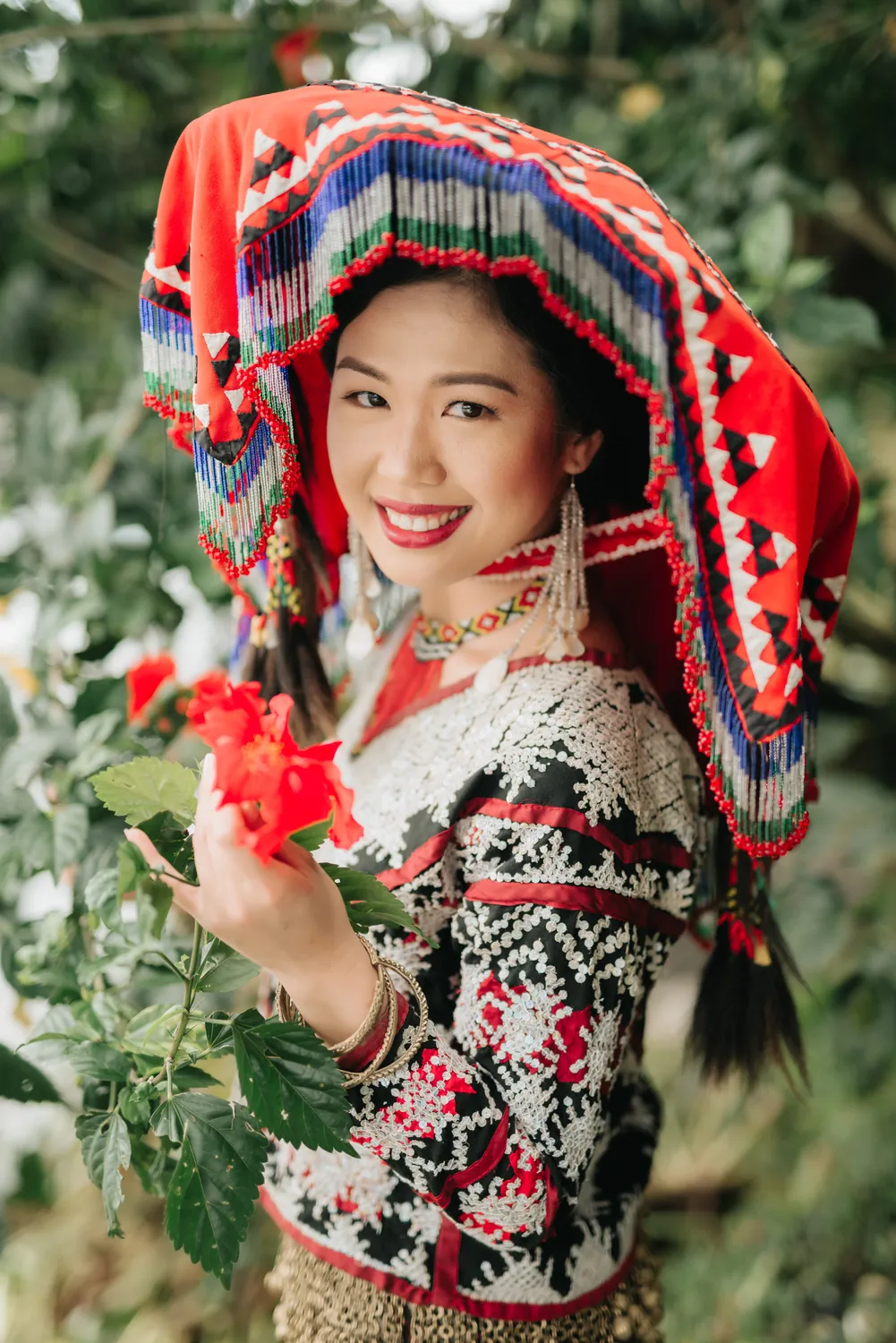 Cecille Castillon-Weinstein in Tboli dress and a red beaded headdress, smiling, holding red flowers