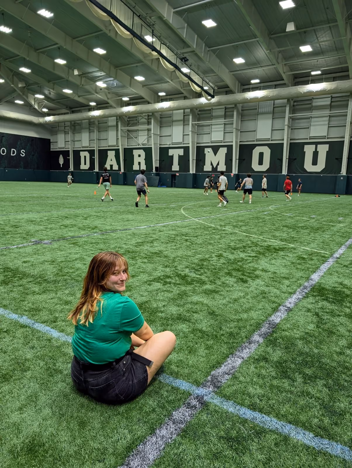 A student on the indoor field with DARTMOUTH on the wall behind her