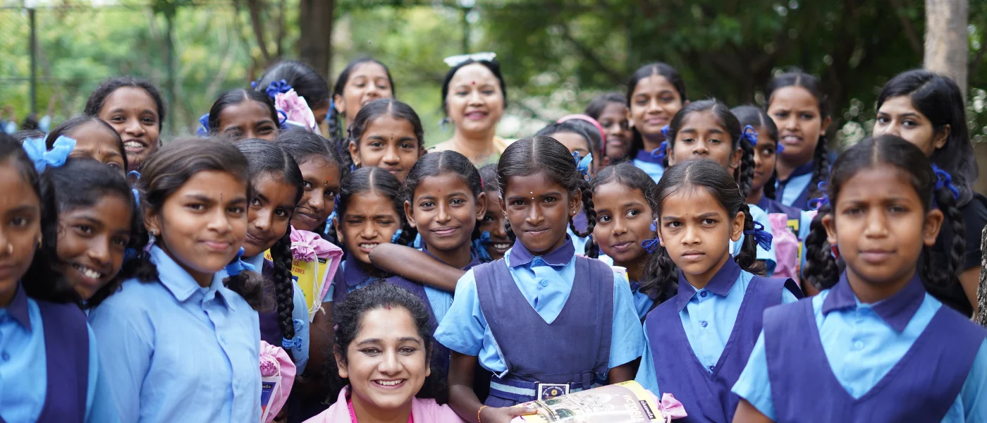 Schoolgirls in blue uniforms, smiling, with a Pinkishe team member