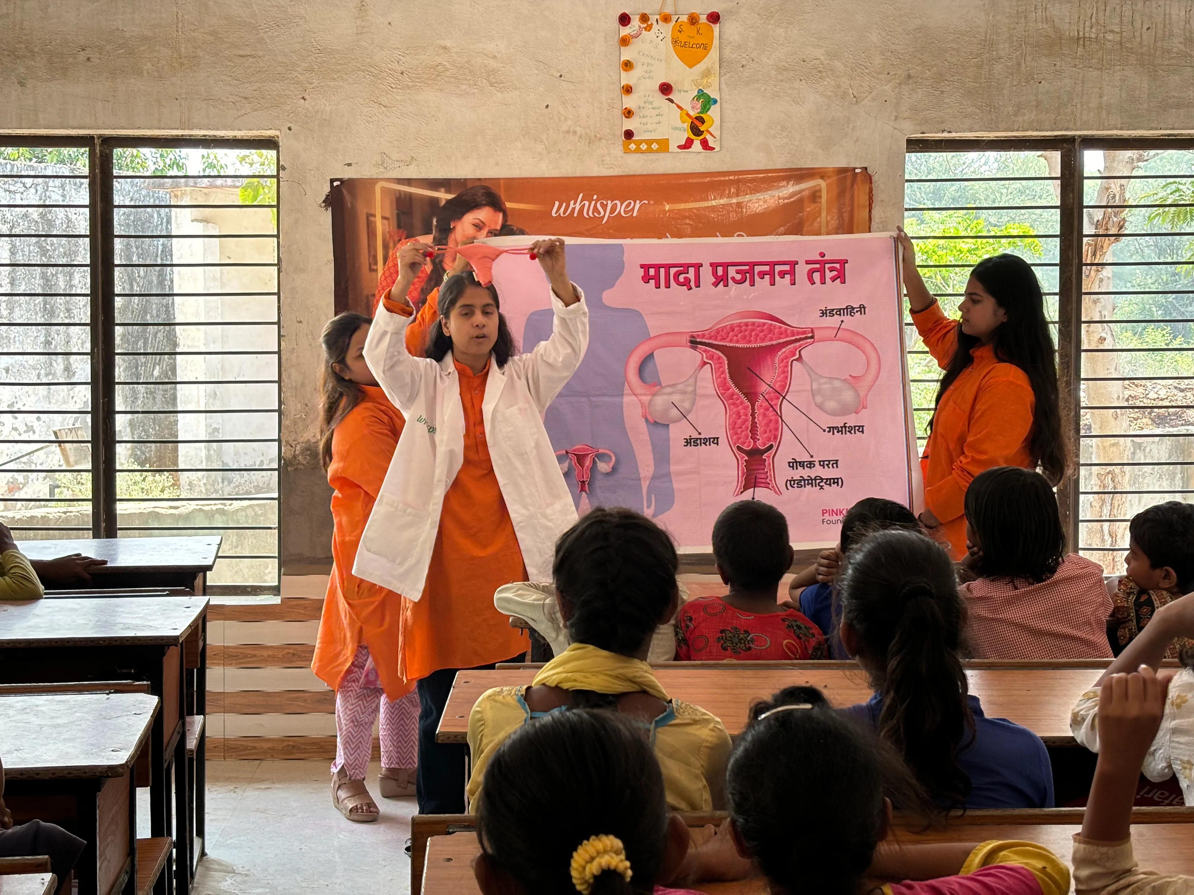 Pinkishe menstrual educators teaching a class of girls with a chart of the reproductive system