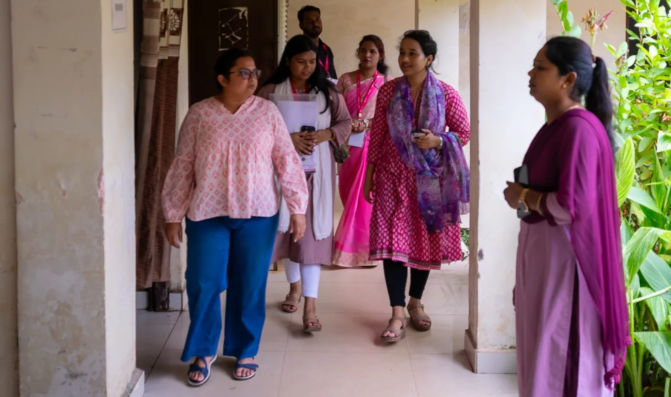 Five Pinkishe team members wearing lanyards walk together along a school corridor