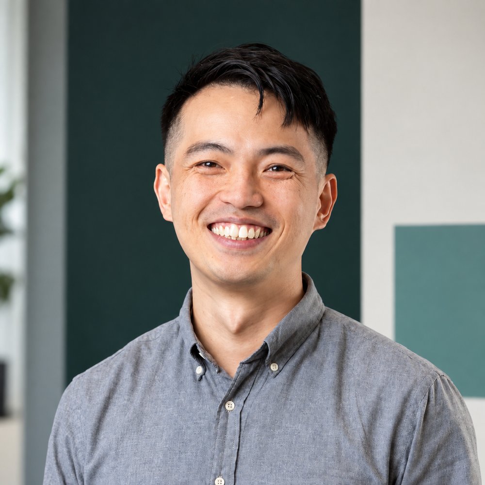 Portrait of Hilfon Tang, smiling, wearing a grey button-down shirt in a bright office.