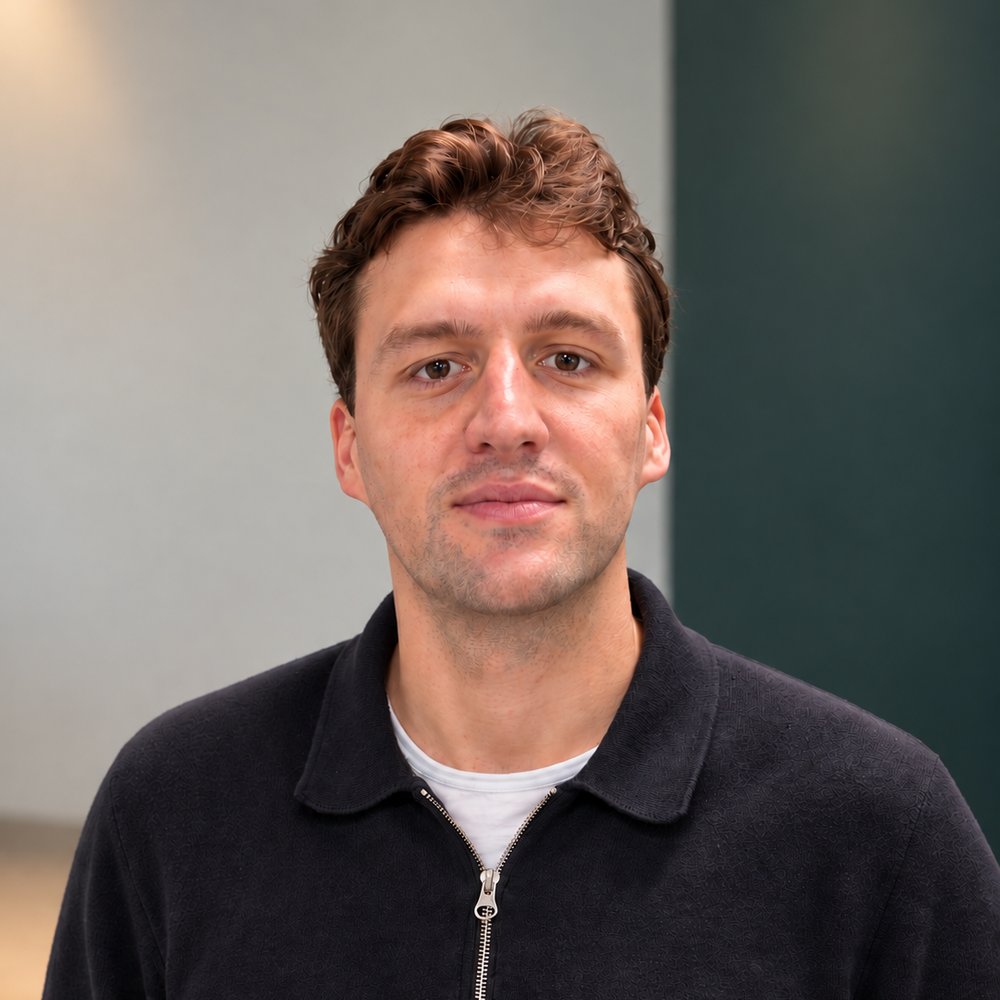 Portrait of Frits van Hulten in a dark zip-up polo shirt, standing in a bright office with a dark green wall.