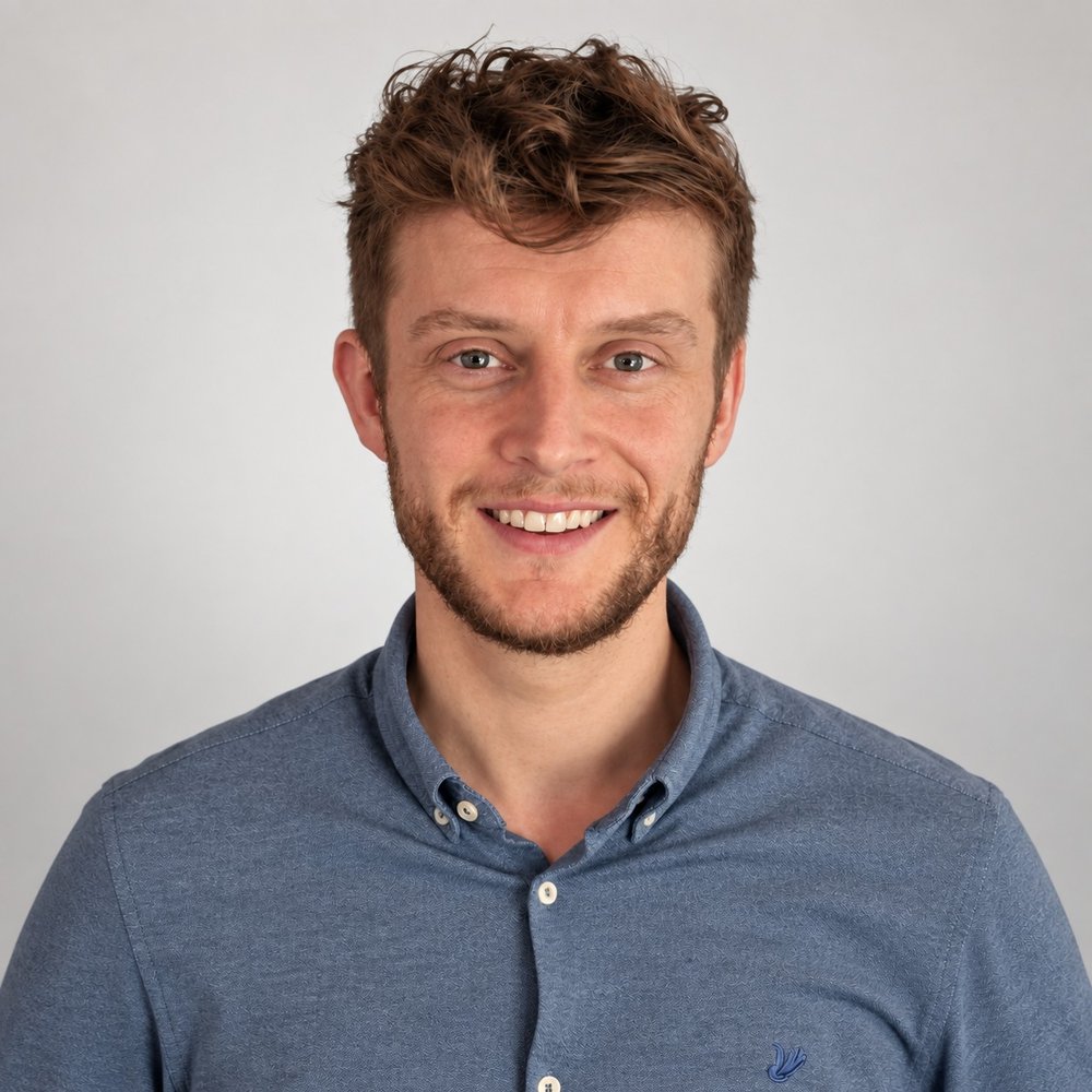 Portrait of Anton Kooij, smiling, wearing a blue button-down shirt against a light grey background.