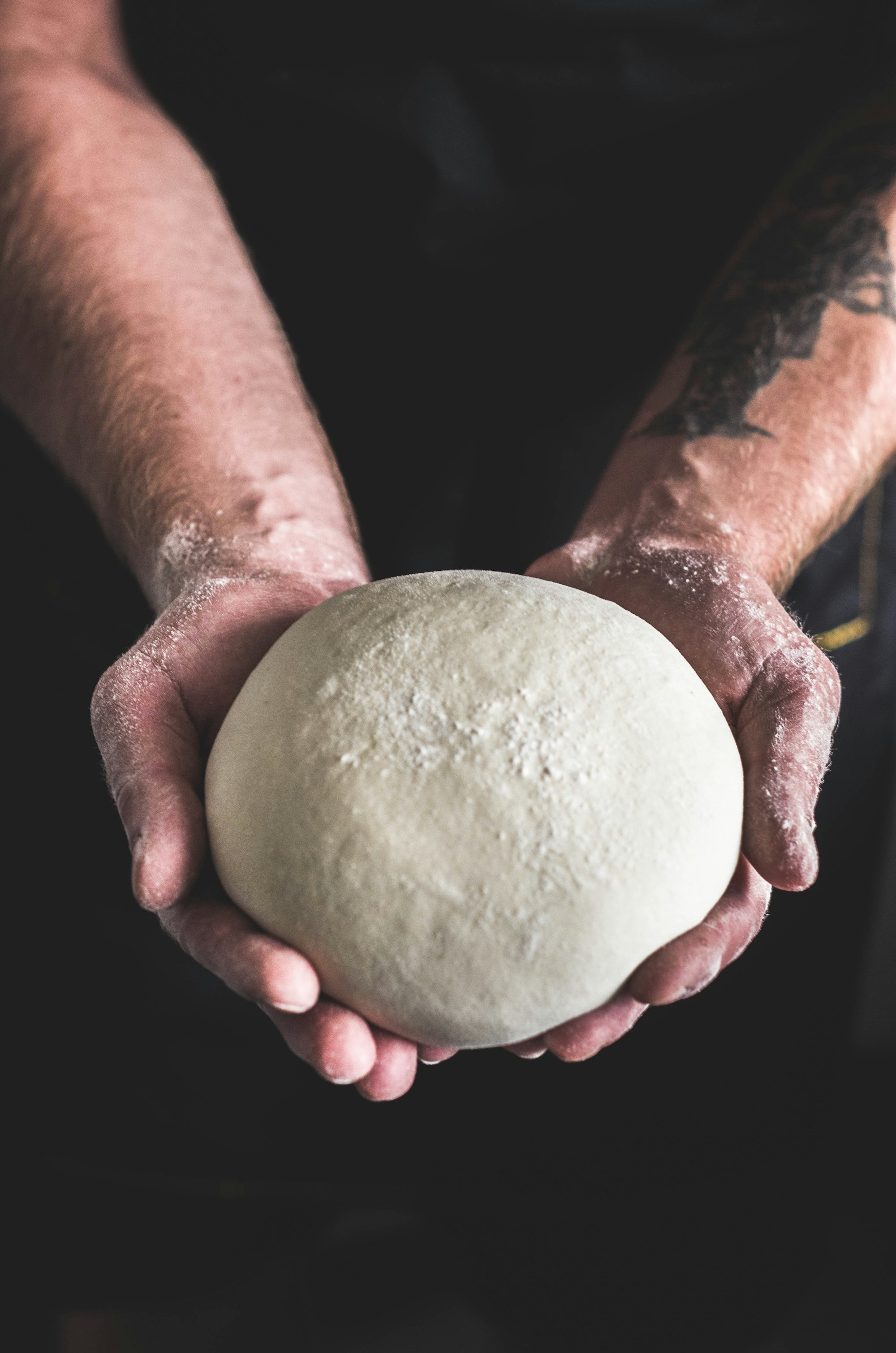 Handen die pizzadeeg uitrekken op een bebloemde werkbank