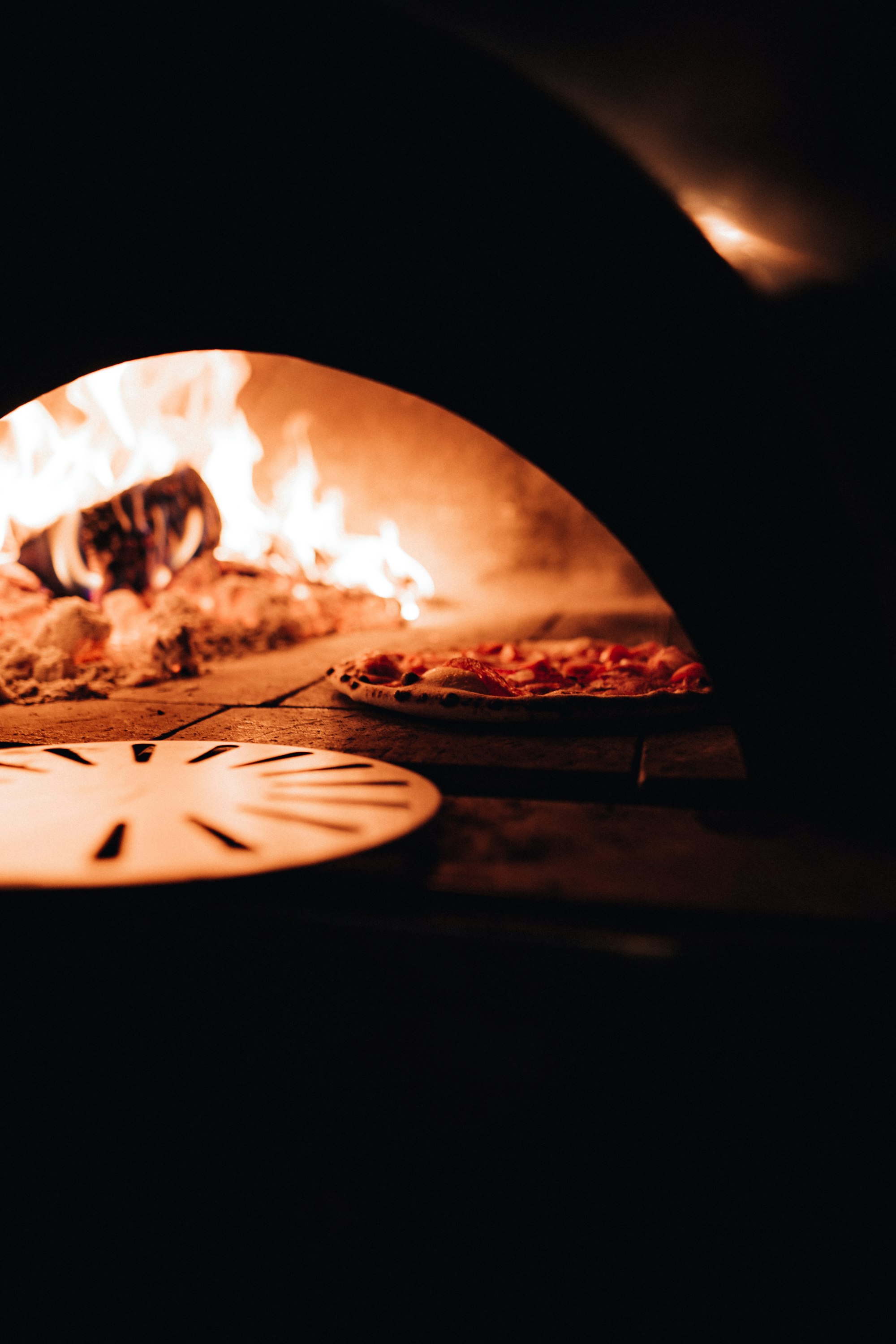 Een pizza in een houtgestookte oven met vlammen op de achtergrond