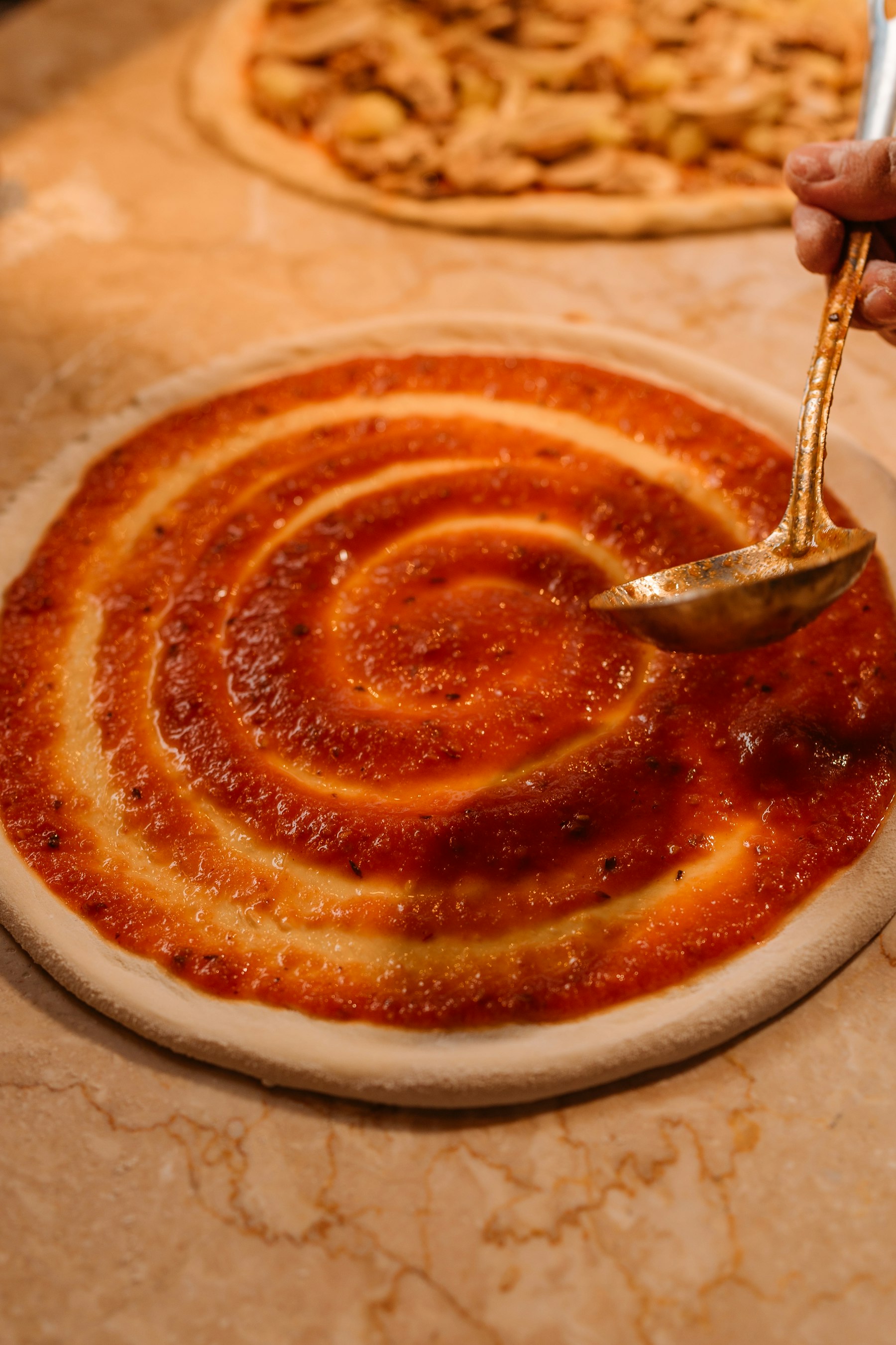 Tomatensaus wordt over de pizzabodem verdeeld