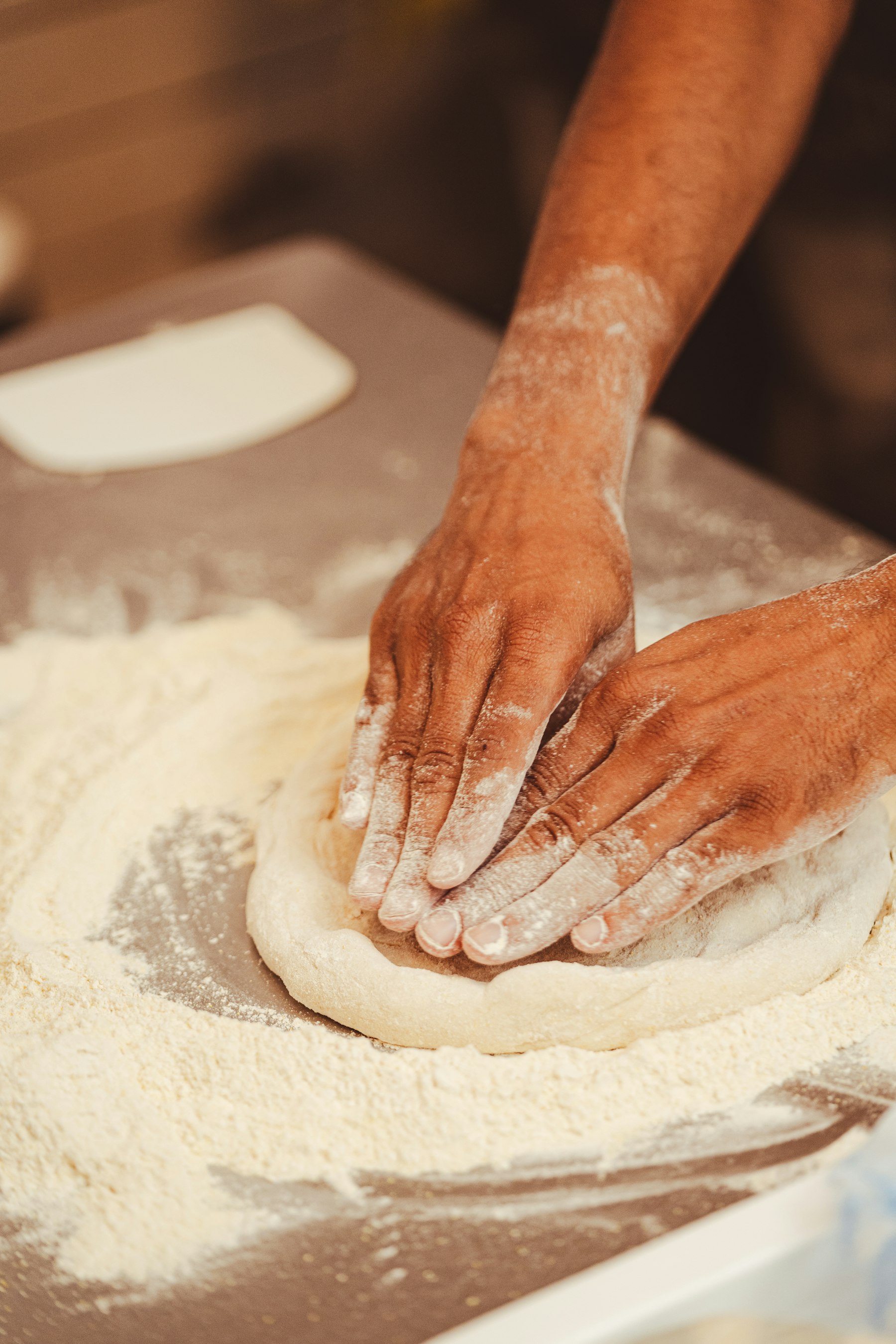 Handen die een bodem pizzadeeg uitrekken op een met bloem bestoven werkblad