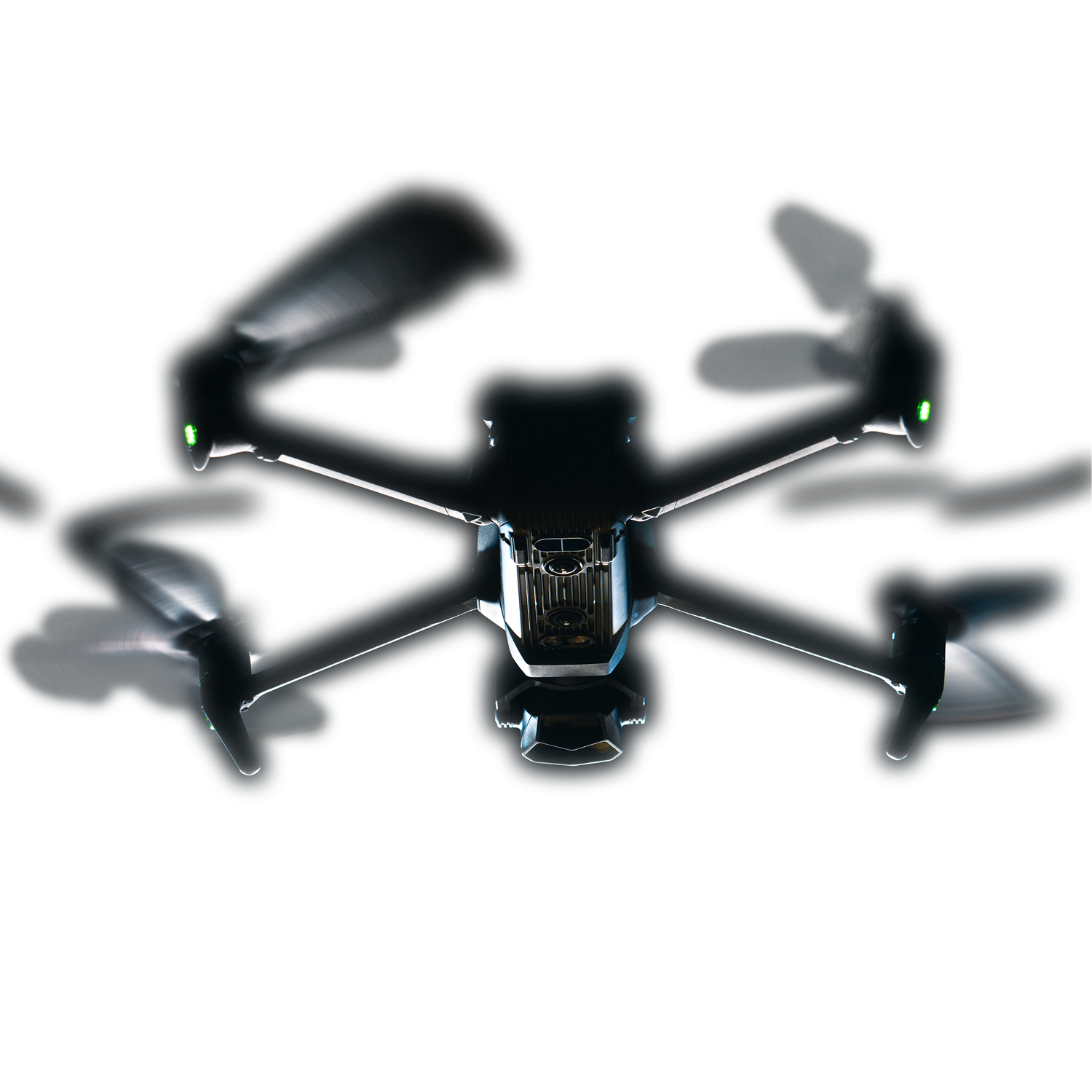 A quadcopter drone with four spinning propellers and green indicator lights hovering against a dark background, viewed from below the front.