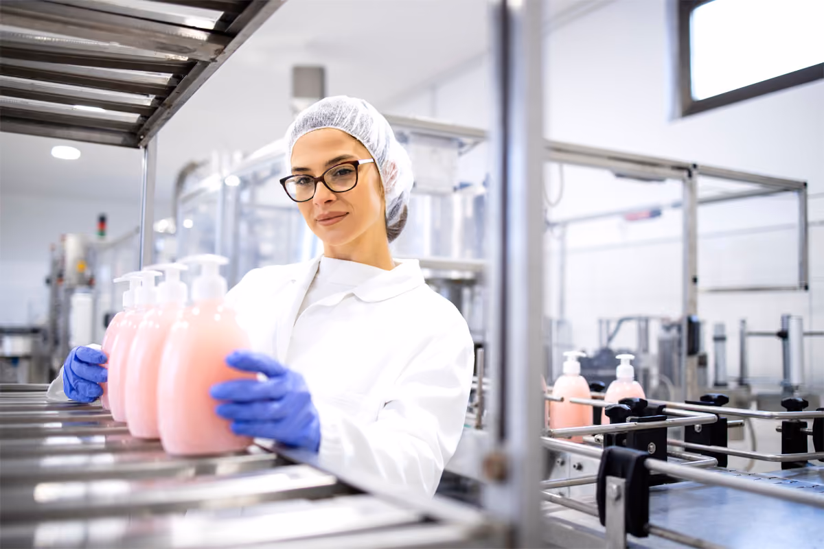 Production worker in a hairnet and gloves checking bottles on a manufacturing line
