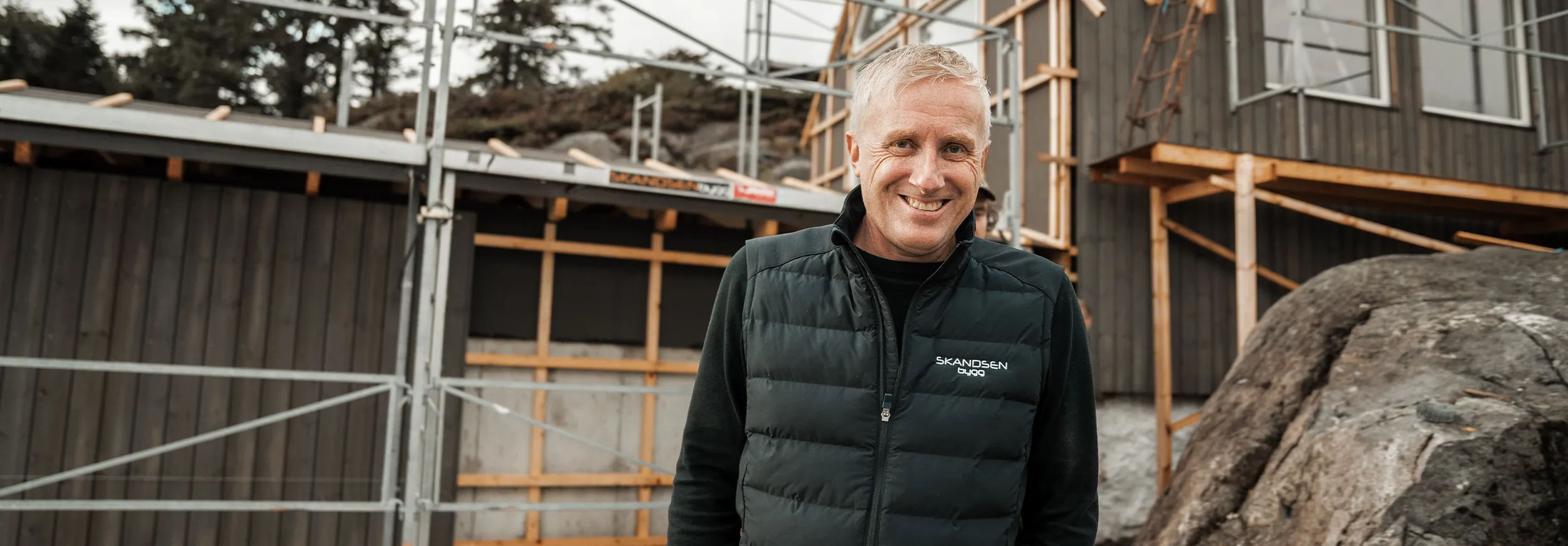 Smilende byggeleder fra Skandsen Bygg foran en hytte under bygging