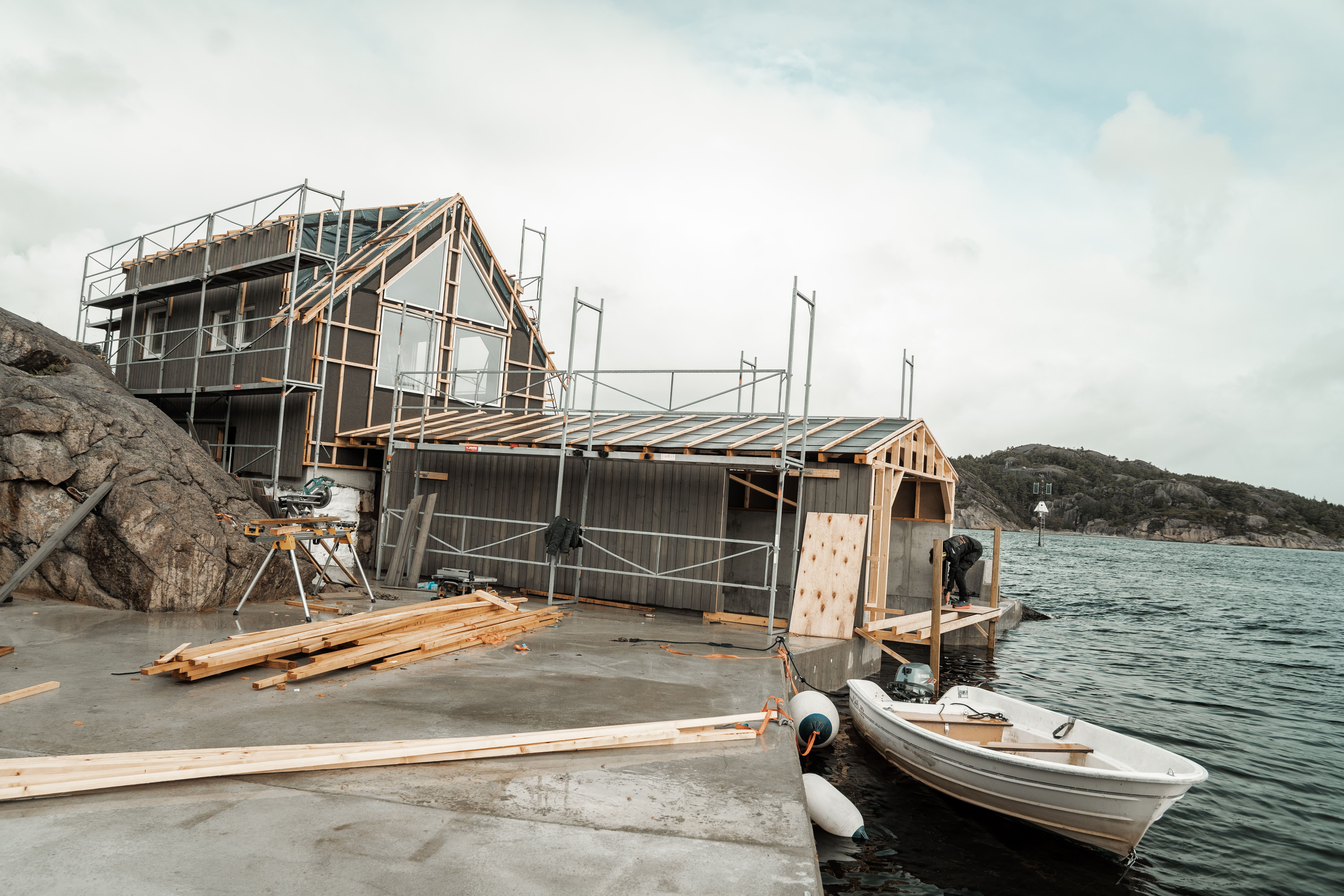 Hytte under bygging ved sjøen med båt i forgrunnen