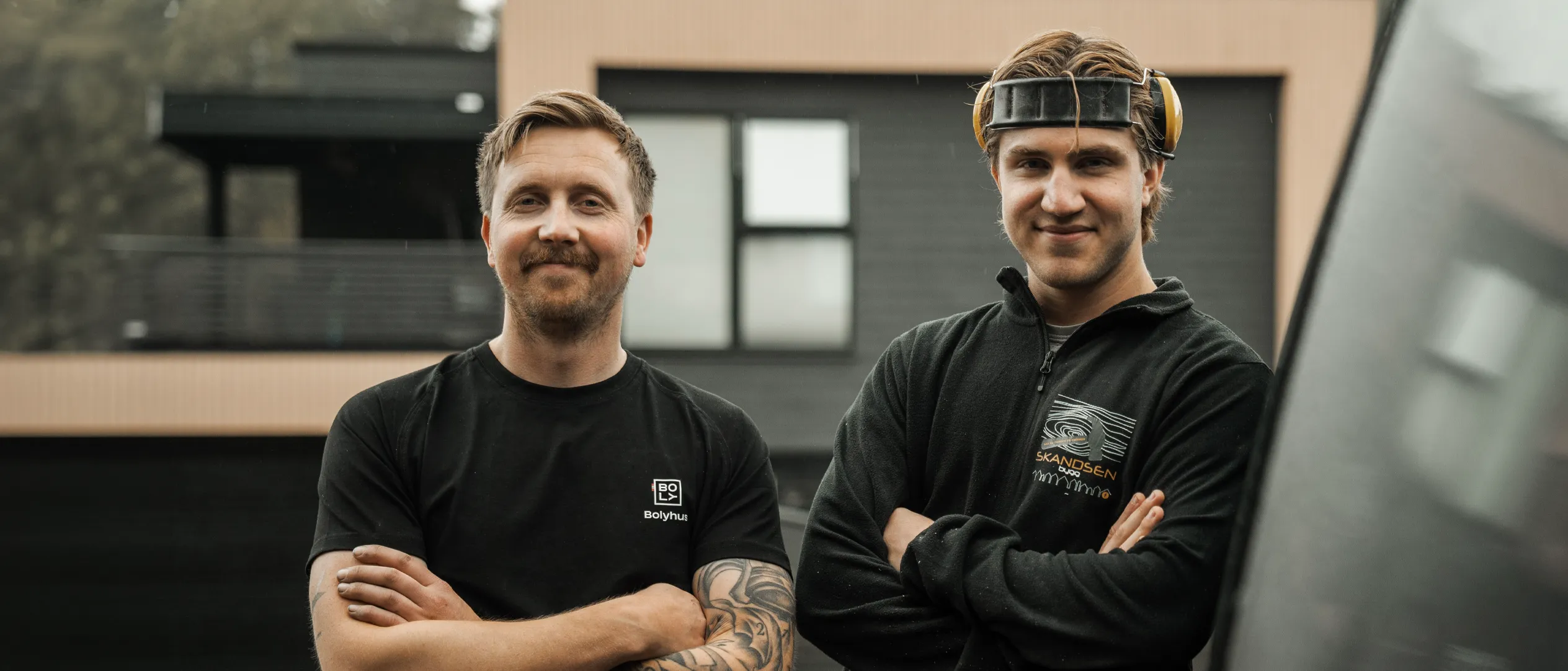 To fra Skandsen Bygg foran et moderne hus med mørk kledning