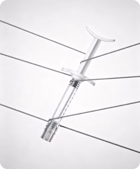 Transparent syringe with a white plunger suspended and entangled among several gray wires against a plain white background.