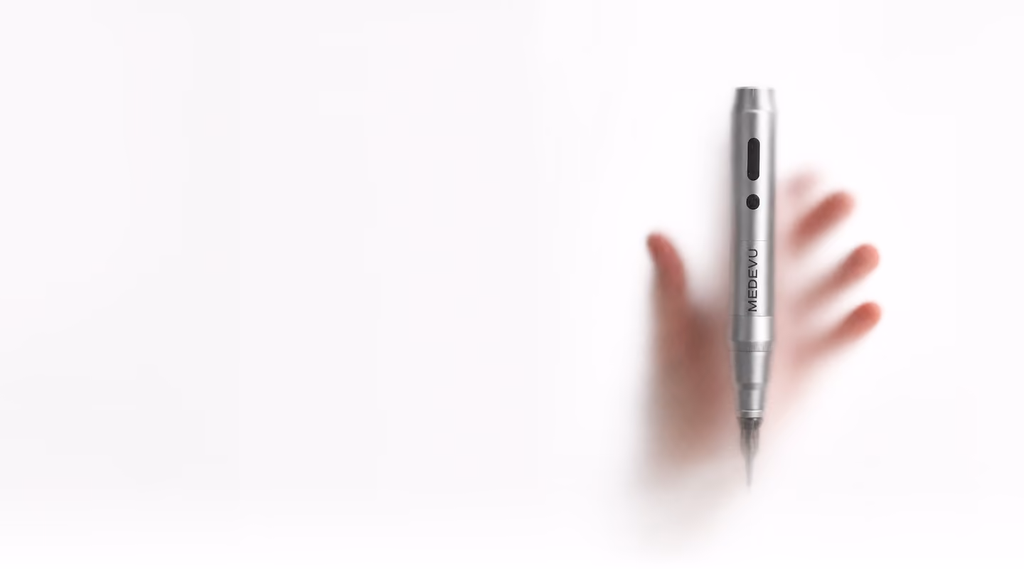 Silver medical or cosmetic pen-like device held against a frosted glass surface with a blurred hand behind it, casting a soft shadow.