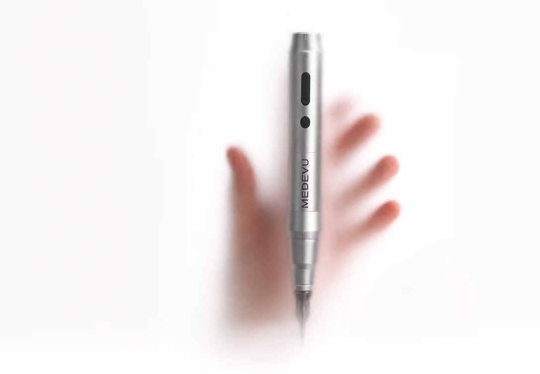 Silver MEDVU device, resembling a pen with buttons, positioned vertically against a frosted surface with a hand blurred behind it.