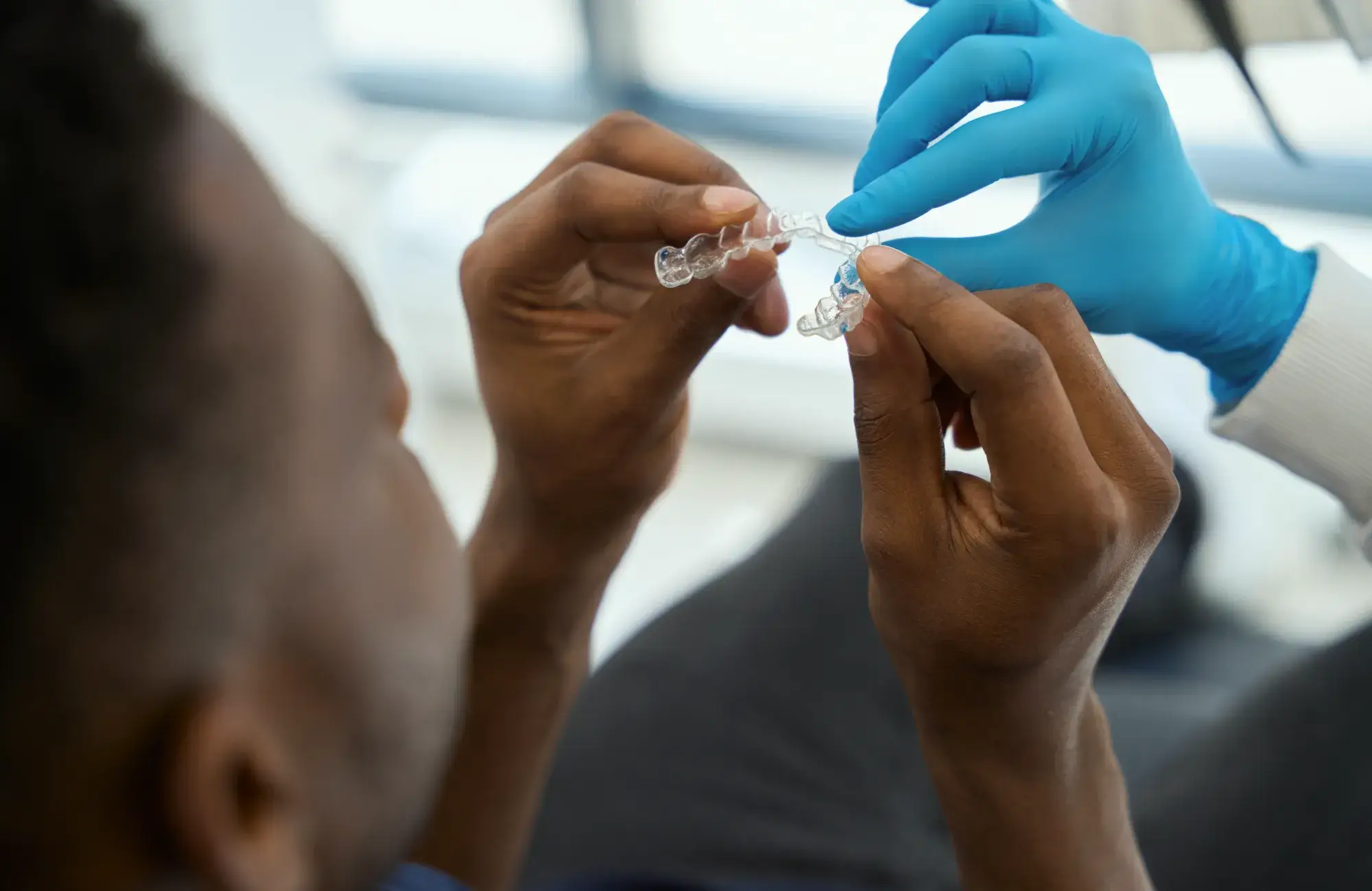 Person holding a clear dental aligner while a gloved hand assists in placing it.
