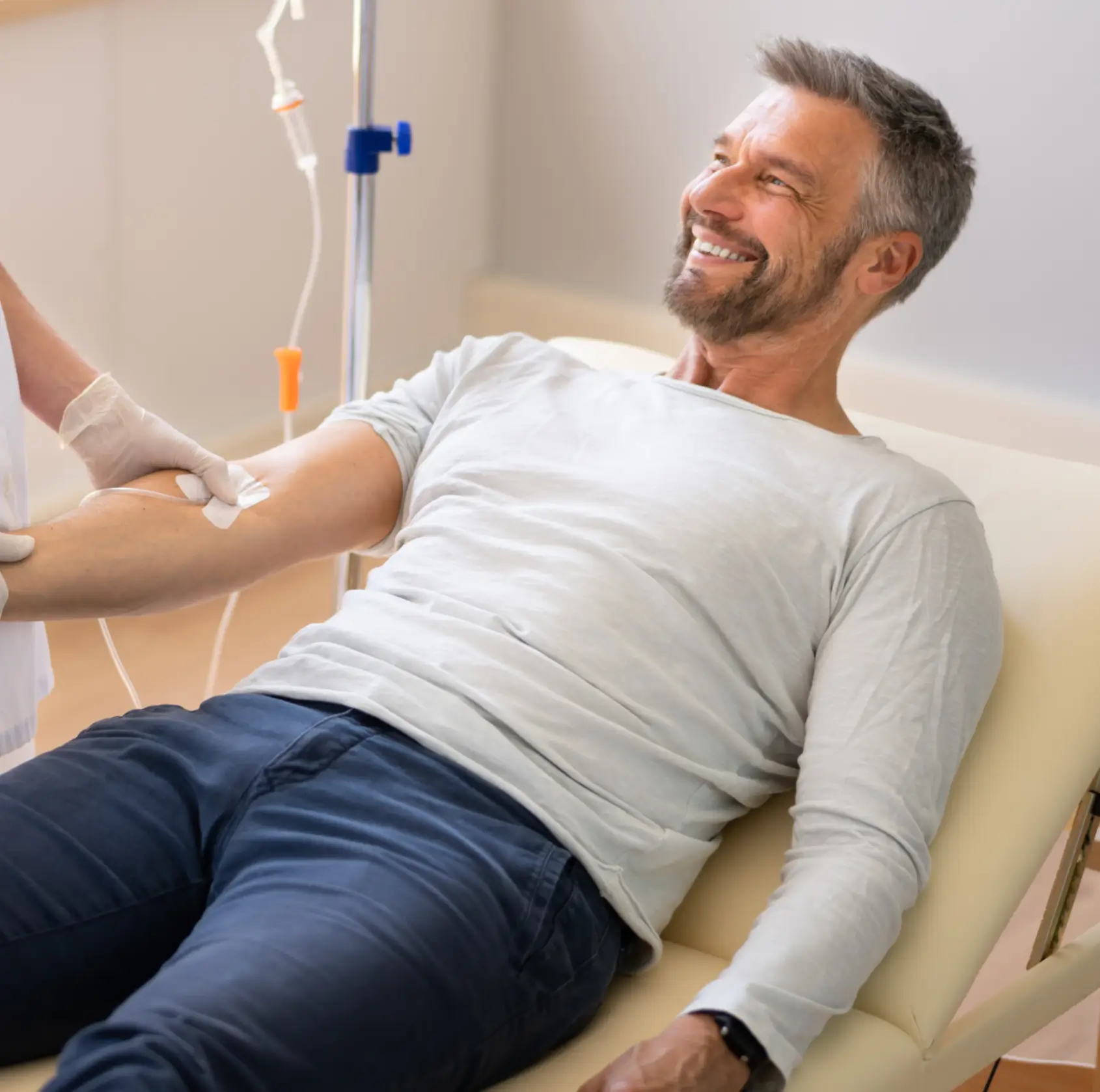 Smiling man receiving intravenous infusion while lying on a medical treatment chair.